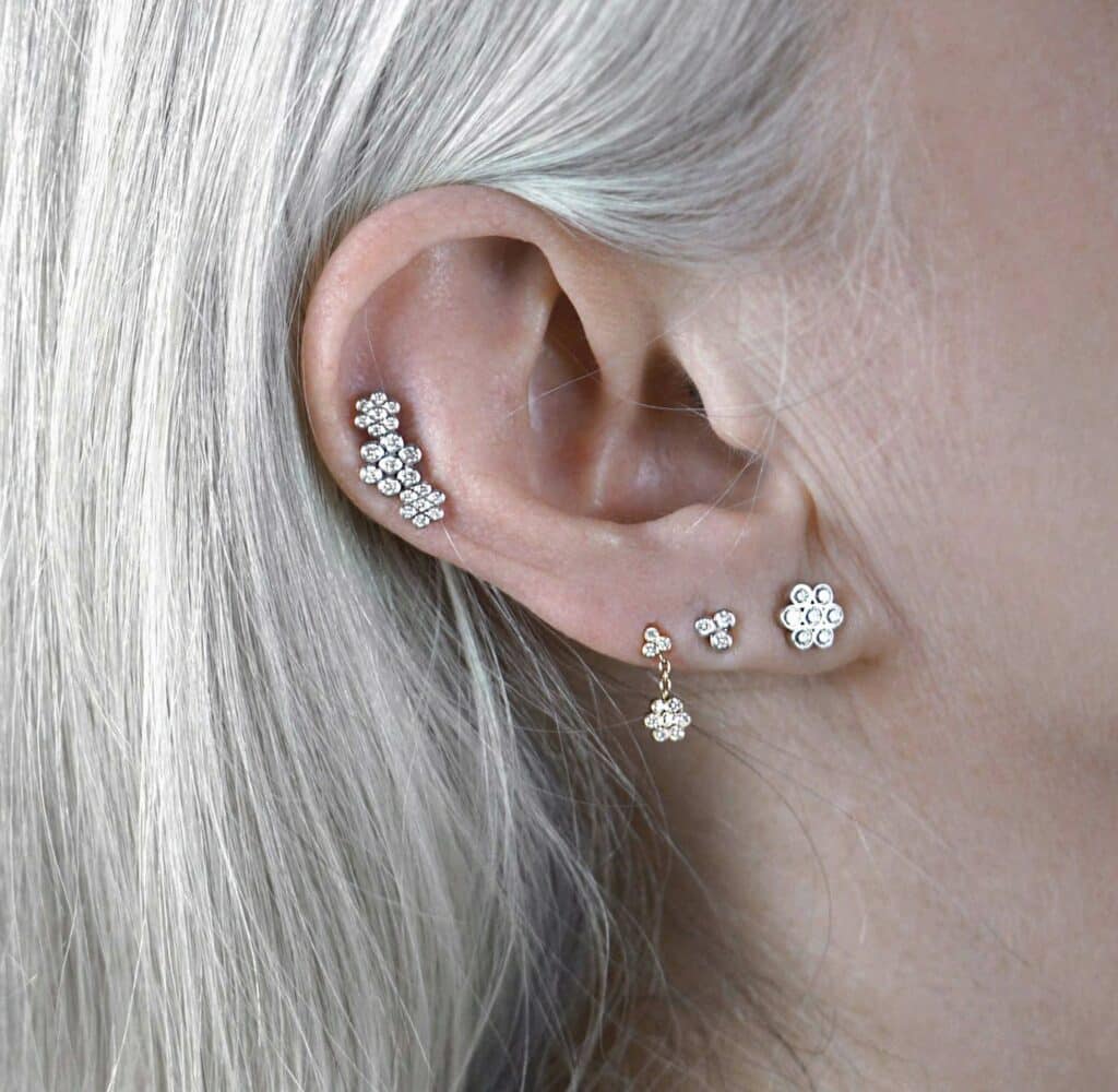 Curated ear with diamond flower studs and helix climber earrings in 18k gold. Lena Cohen London fine piercing jewellery.